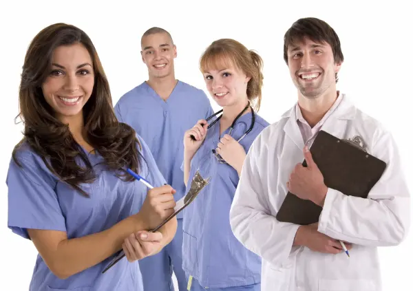 Gruppe von vier medizinischen Fachkräften, drei in blauen Kitteln, eine in weißem Kittel mit Klemmbrett und Stift.