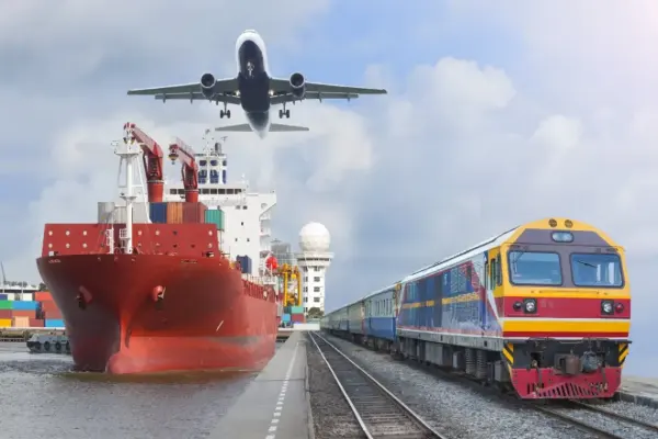 Rotes Frachtschiff im Hafen, gelb-blauer Zug auf Gleisen rechts, Passagierflugzeug im Landeanflug darüber.