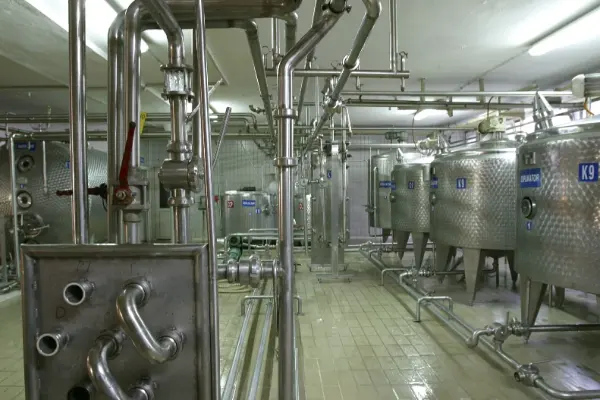 Industrieller Raum mit mehreren großen, zylindrischen Edelstahltanks und vernetzten Rohrleitungen an der Decke und Wand.