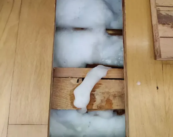 Schaum quillt aus einer Lücke zwischen hellen Holzdielen mit sichtbarer Maserung.